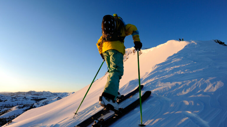 A skier skinning up a snow covered slope at sunrise in the Sierra Nevada near Lake Tahoe, California.