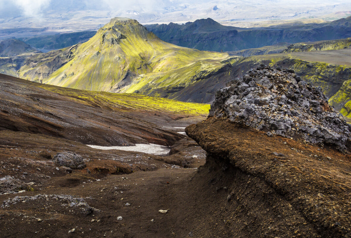 Hiking on Fimmvorduhals in summer: View over a landscape of bizarre lava formations, left over snow, moss covered mountains and the beautiful valley of Thorsmork in the distance.