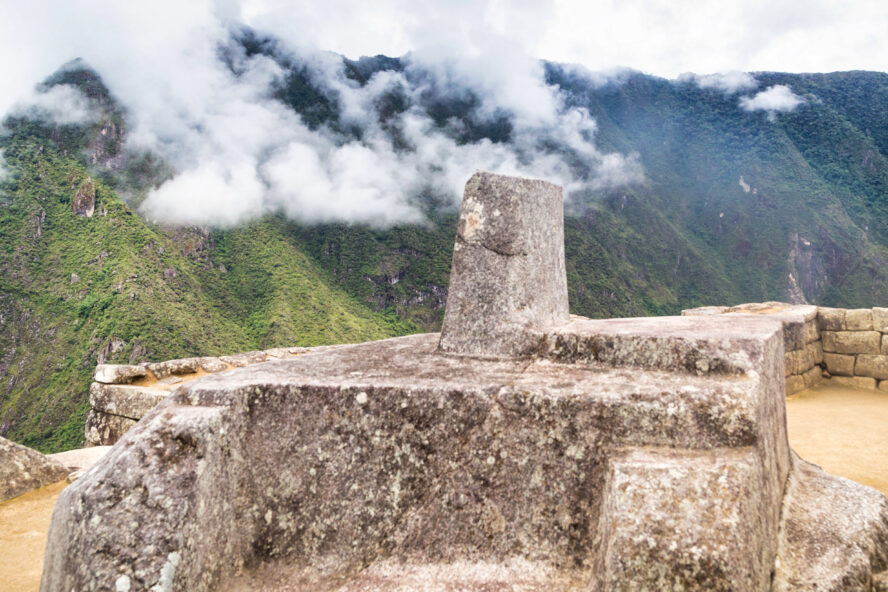 A close-up look at the ceremonial stone located in Machu Picchu with the ever-present clouds in the background.