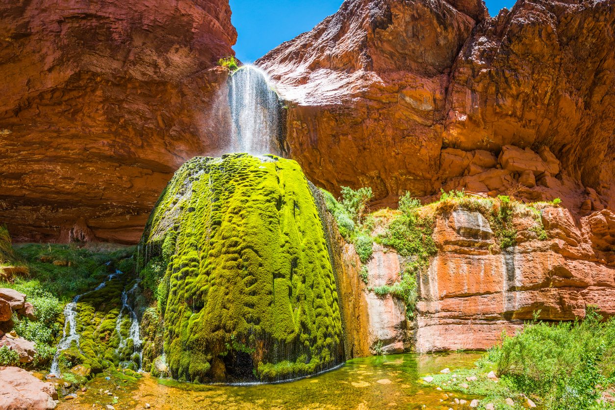 Waterfall cascading over the rocky rim of the Bright Angel Canyon into the mossy green oasis of Ribbon Falls deep in the desert wilderness of the Grand Canyon National Park, Arizona, USA.