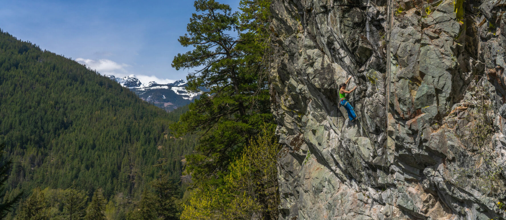 A climber climbing in Squamish with a panoramic view of a mountain as the backdrop