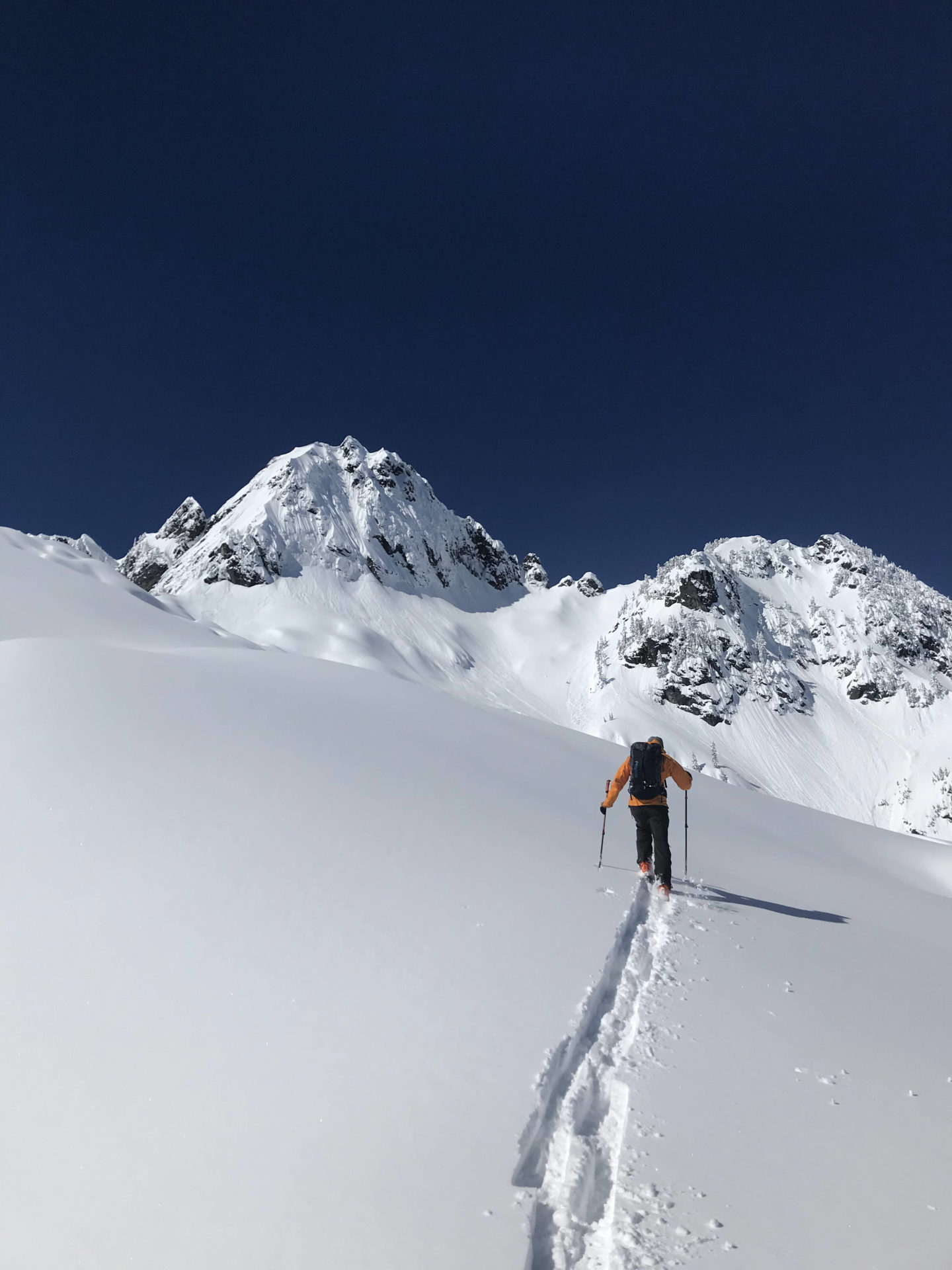 A backcountry skier moving through untracked snow in Snoqualmie with two snow-dusted mountain peaks in the distance.