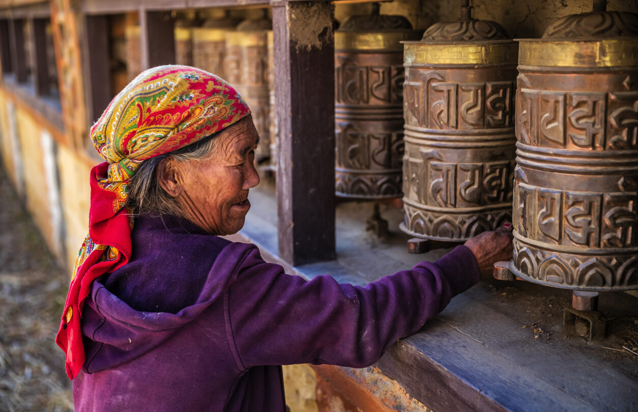 Old Tibetan woman turning the prayer wheels in a small village, Upper Mustang. Mustang region is the former Kingdom of Lo and now part of Nepal, in the north-central part of that country, bordering the People's Republic of China on the Tibetan plateau between the Nepalese provinces of Dolpo and Manang.