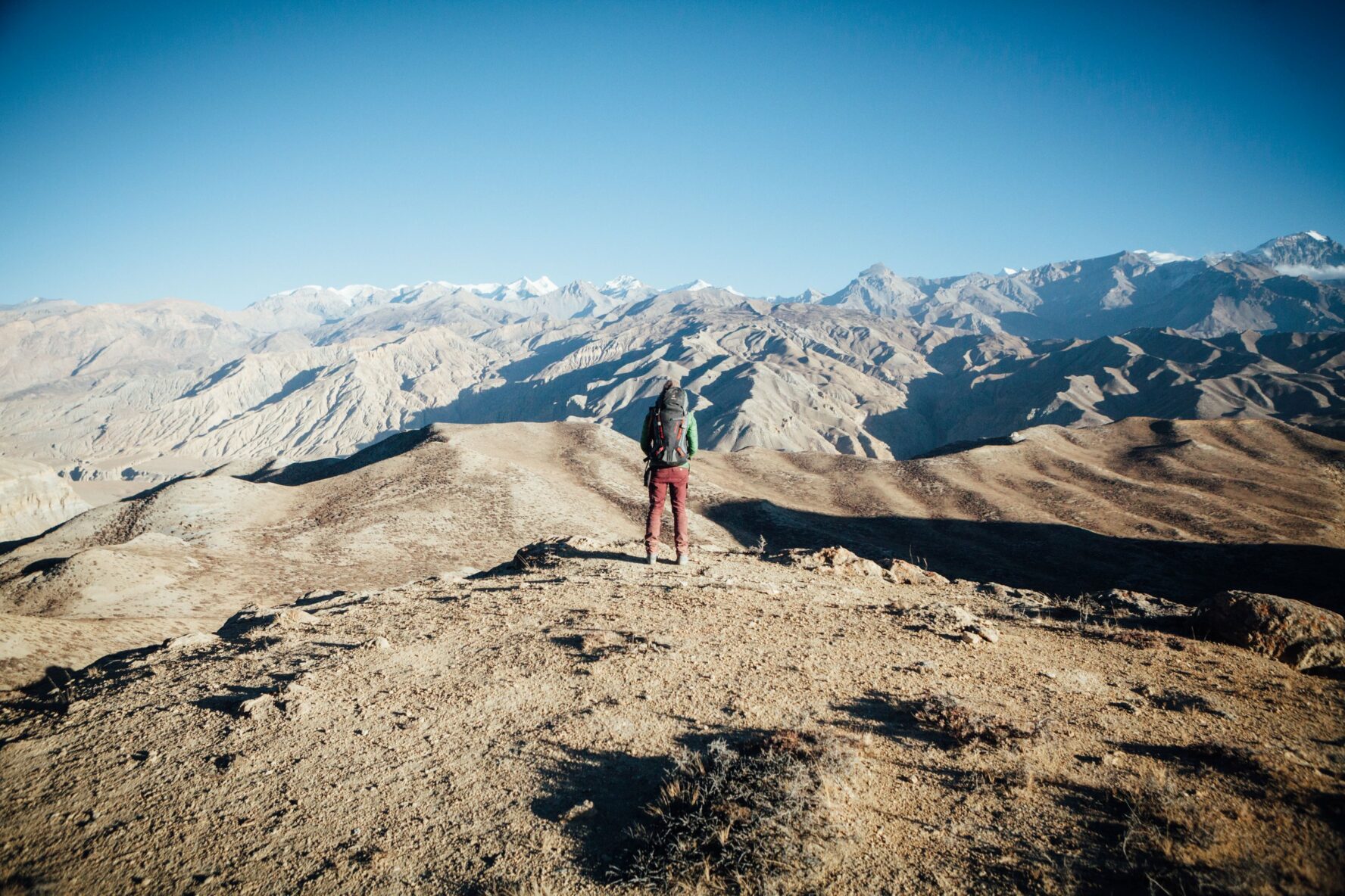 A hiker standing on a trail and looking in the distance. White and beige hills spruce up in the background
