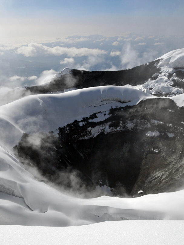 Mountain climber in Cotopaxi descending into a sea of clouds and Antisana volcano in the background, Andes Ecuador