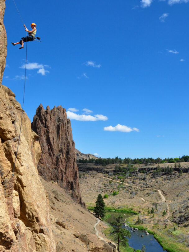 A woman nears the top of a spire at Smith Rock State Park, Oregon. The Crooked River is far below in the valley.