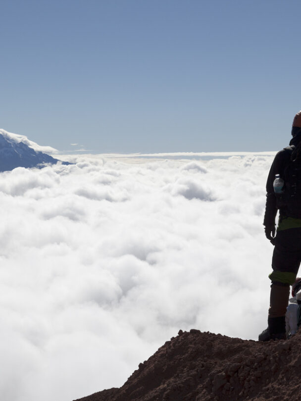 Mountain climber in Cotopaxi descending into a sea of clouds and Antisana volcano in the background, Andes Ecuador