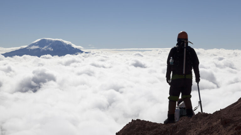 Mountain climber in Cotopaxi descending into a sea of clouds and Antisana volcano in the background, Andes Ecuador