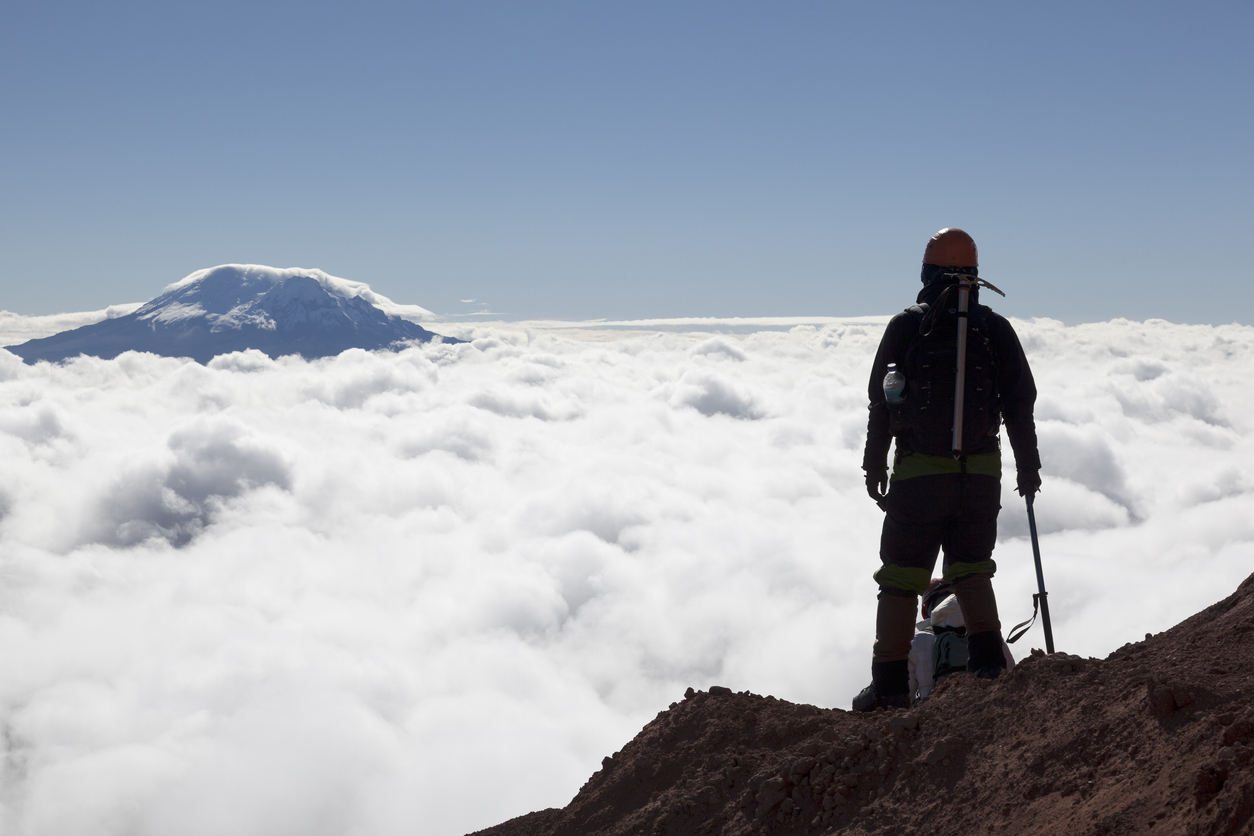 Mountain climber in Cotopaxi descending into a sea of clouds and Antisana volcano in the background, Andes Ecuador