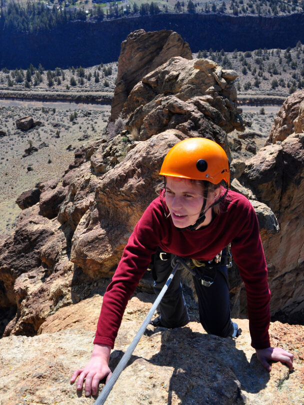 A woman nears the top of a spire at Smith Rock State Park, Oregon. The Crooked River is far below in the valley.