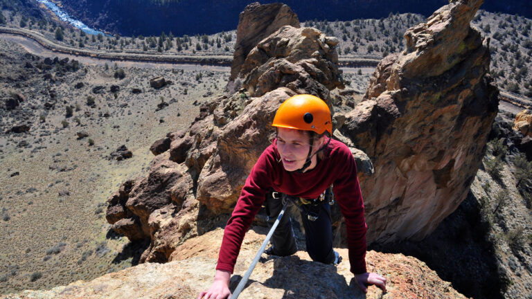 A woman nears the top of a spire at Smith Rock State Park, Oregon. The Crooked River is far below in the valley.