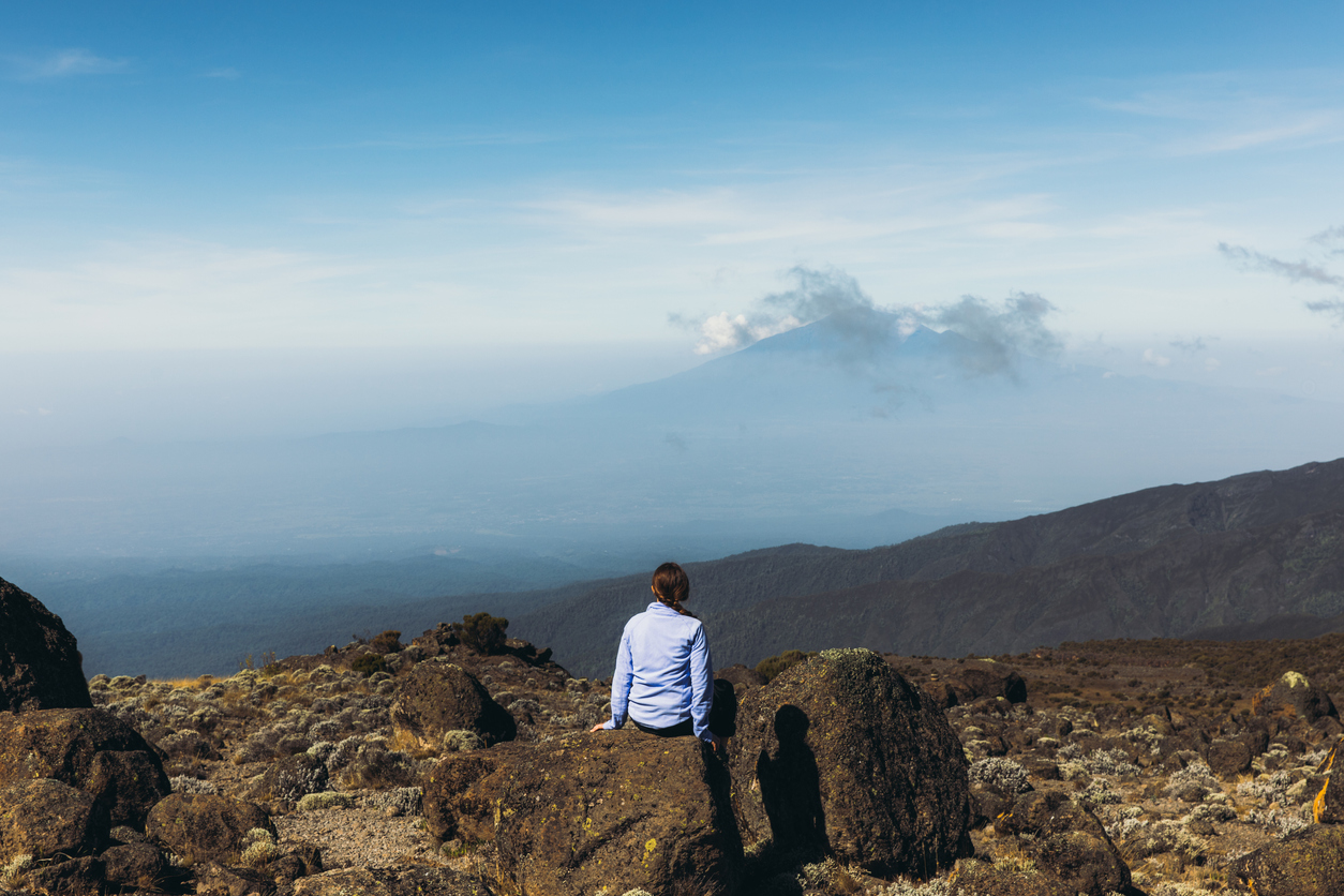 Woman traveler relaxing after the hiking trip feeling success enjoying the view of the Meru mountain from the Mount Kilimanjaro, Tanzania