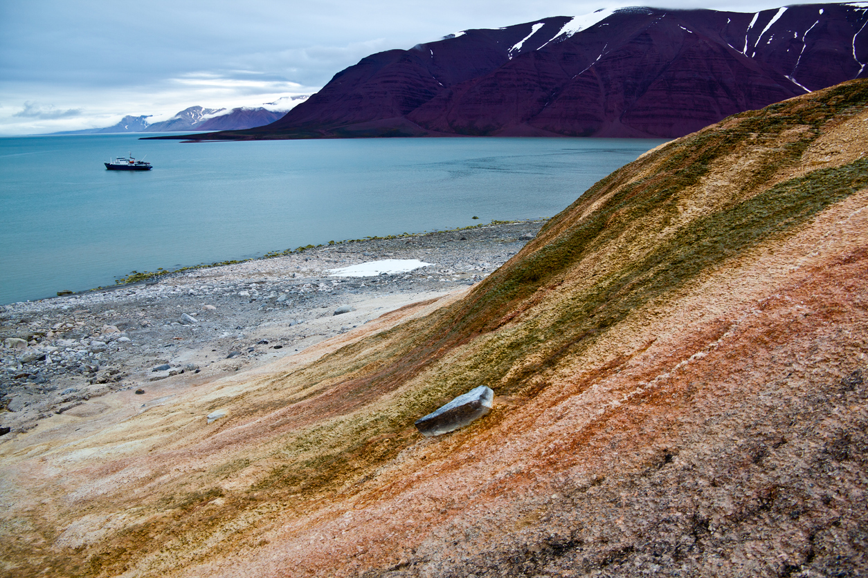 Arctic landscape in Spitzbergen -Svalbard. View across the Bockfjord to the mountains on the other side of the Fjord. Passenger cruise in anchoring in the Fjord. Hot springs with colored rocks in the foreground.