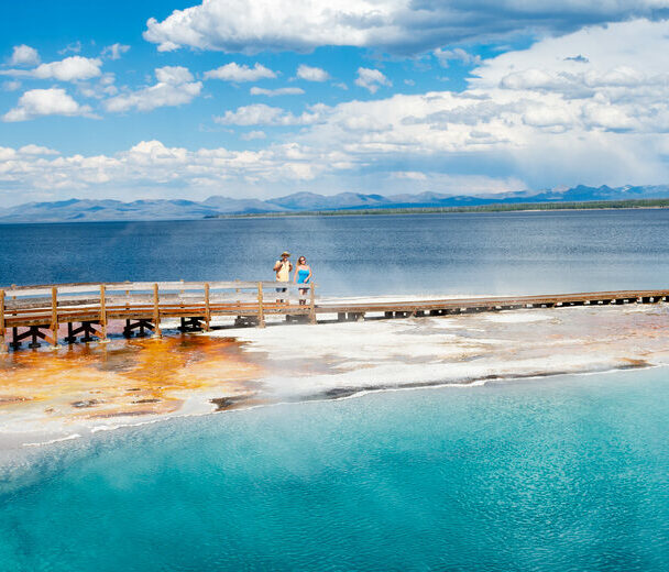Couple relaxing and enjoying beautiful view of hot spring on vacation hiking trip. Beautiful Yellowstone Lake in the background and hot spring in foreground. Yellowstone National Park. Wyoming, USA