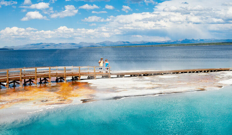Couple relaxing and enjoying beautiful view of hot spring on vacation hiking trip. Beautiful Yellowstone Lake in the background and hot spring in foreground. Yellowstone National Park. Wyoming, USA