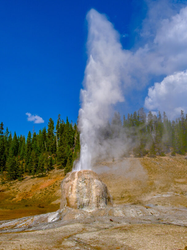 Couple relaxing and enjoying beautiful view of hot spring on vacation hiking trip. Beautiful Yellowstone Lake in the background and hot spring in foreground. Yellowstone National Park. Wyoming, USA