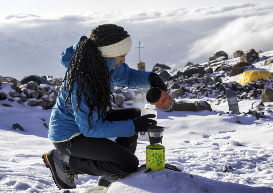 A mountaineer pours the leftover warm water from cooking with her camp stove into her water bottle.