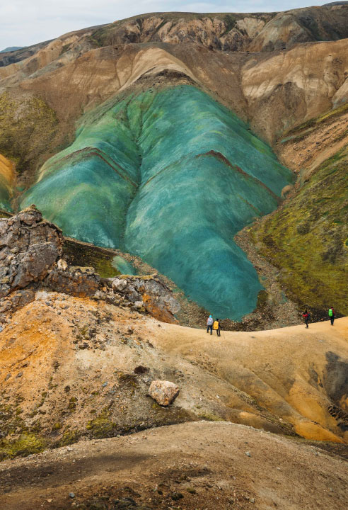 Group of hikers standing under Grænihryggur, Iceland's surreal mountain ridge of emerald glass