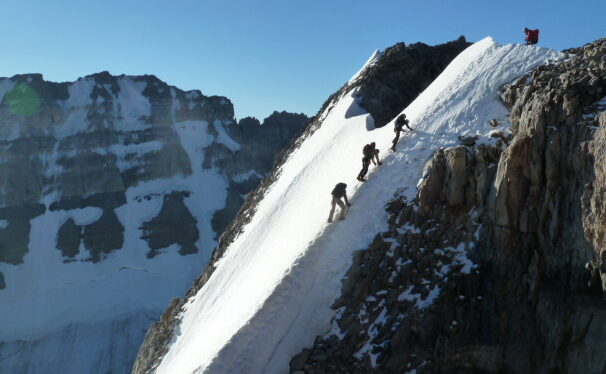 Three alpine climbers summiting a snowy peak