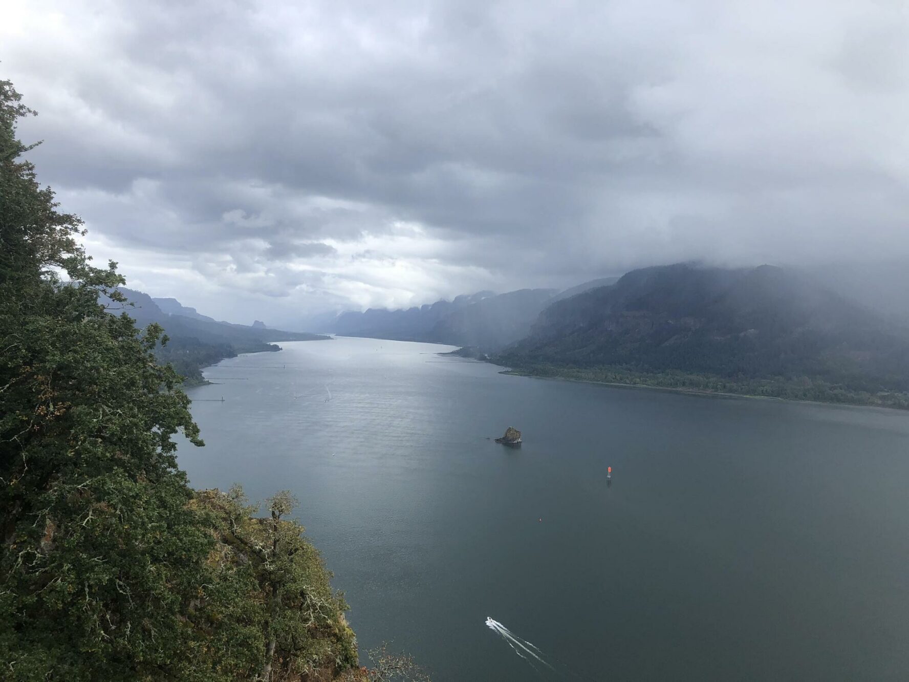 The Columbia River Gorge on a misty day in the spring with a small boat crossing the wide river.