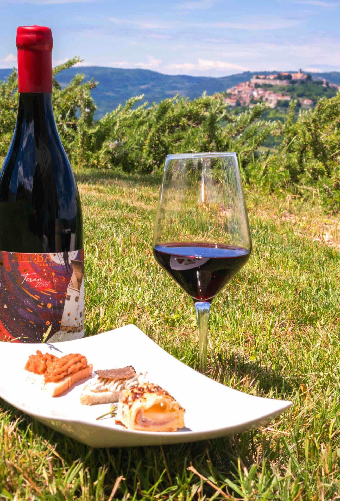 A bottle of Istrian red wine and a plate with snacks with a view of Motovun in the background.