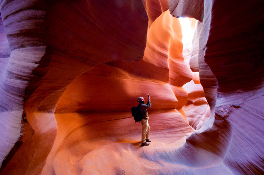 A hiker taking photos of the smooth and wavy sandstone walls inside Antelope Canyon
