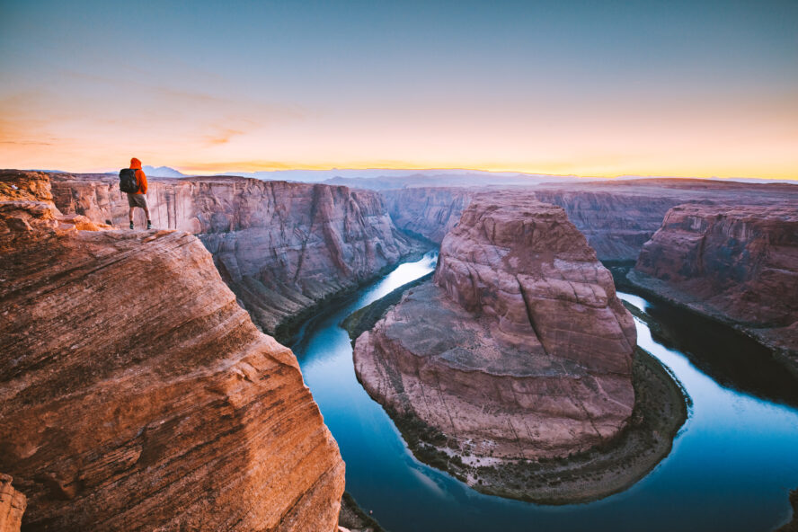 A hiker standing on the edge of a cliff overlooking Horseshoe Bend.