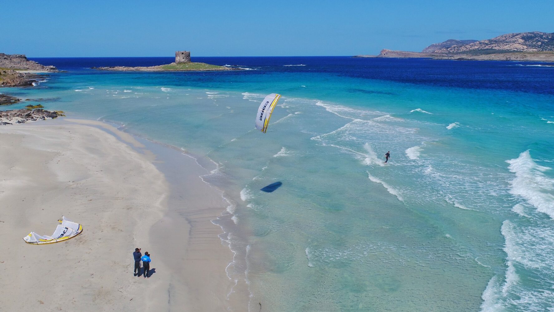 Kitesurfers surfing on the blue sea near a sandy beach