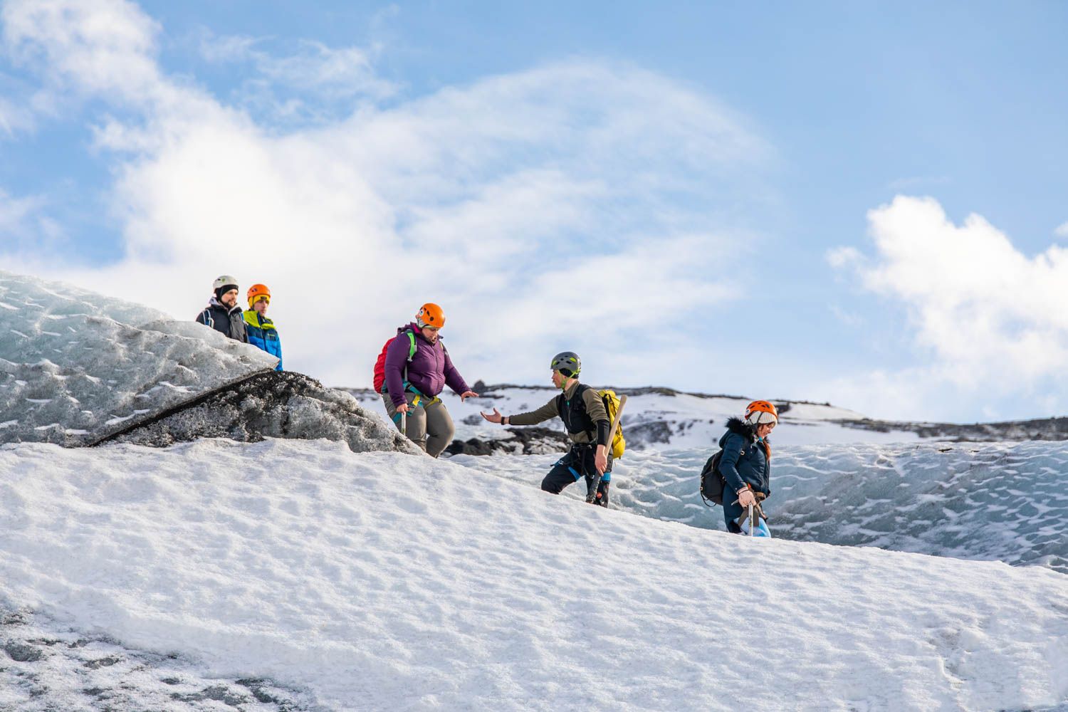 One hiker giving a helping hand to another as they walk on the glacier