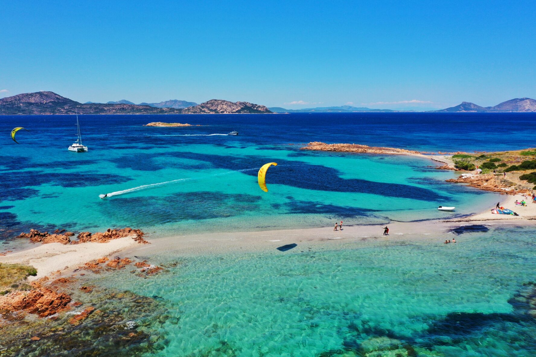 Vivid teal sea and kitesrufers near a sandy beach in Italy