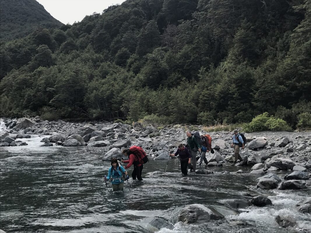 Hikers wading a river in New Zealand