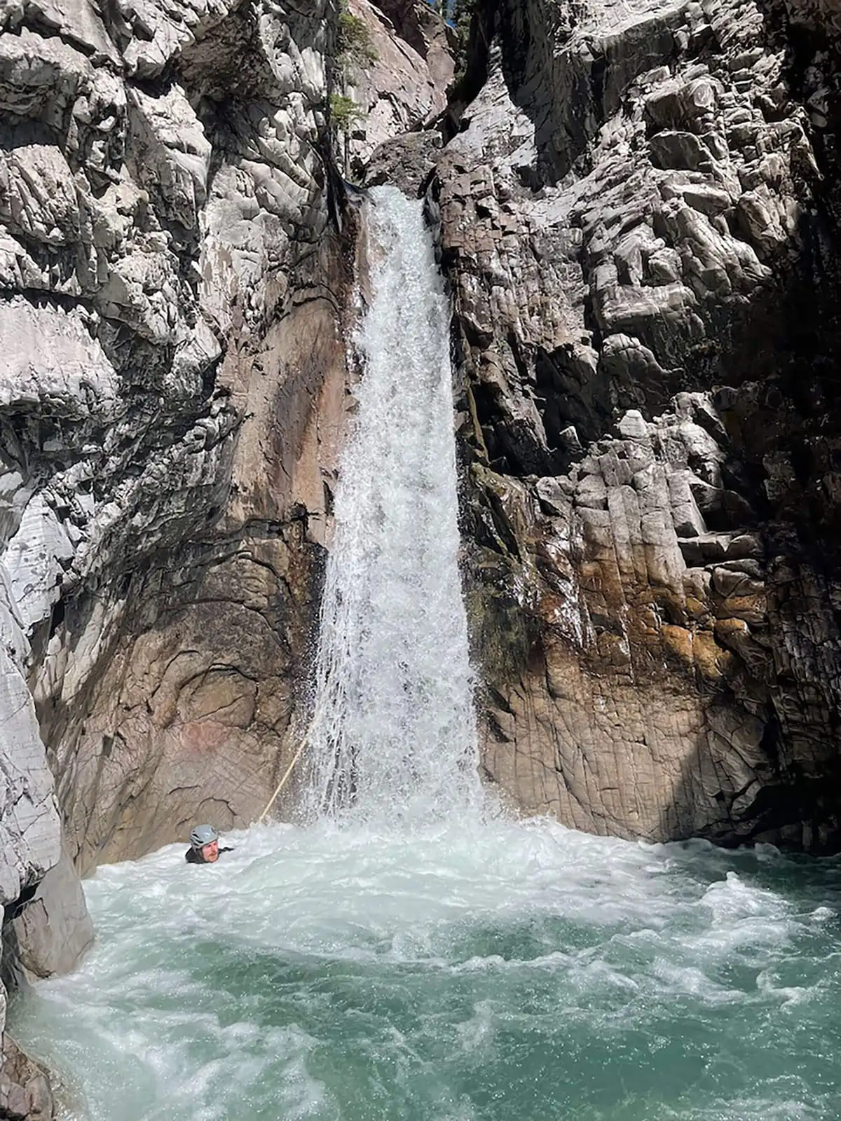 One of many waterfalls in Bear Creek and a canyoneer swimming underneath it.