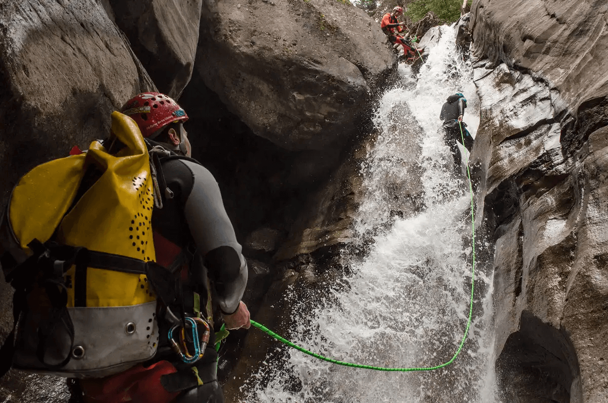 The man at the bottom of the waterfall on the left side of the image is watching two other people as they are climbing.