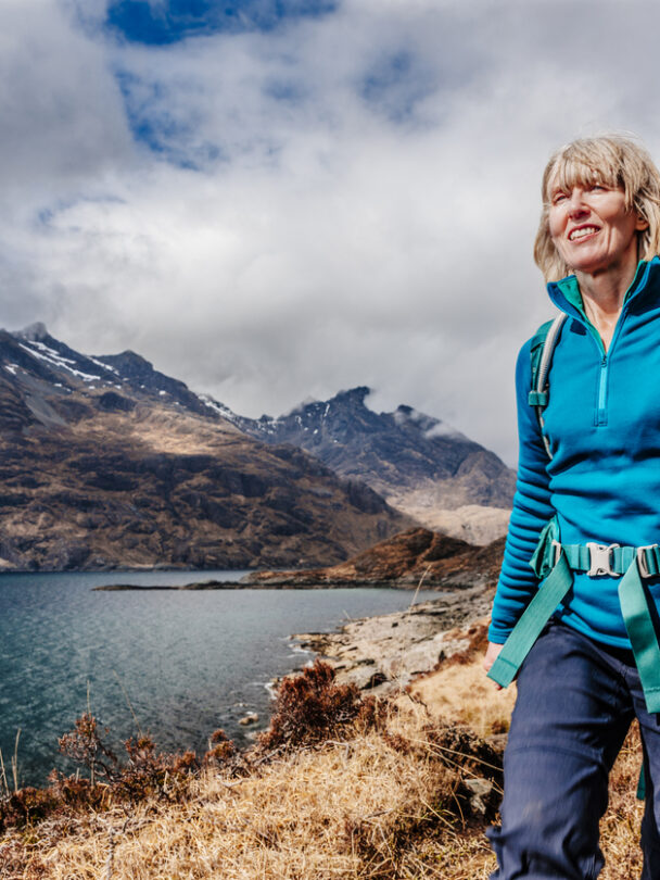 A smiling hiker walking along the shore of Loch Coruisk, the Cuillin Hills in the background