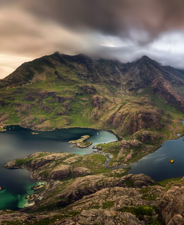 A smiling hiker walking along the shore of Loch Coruisk, the Cuillin Hills in the background