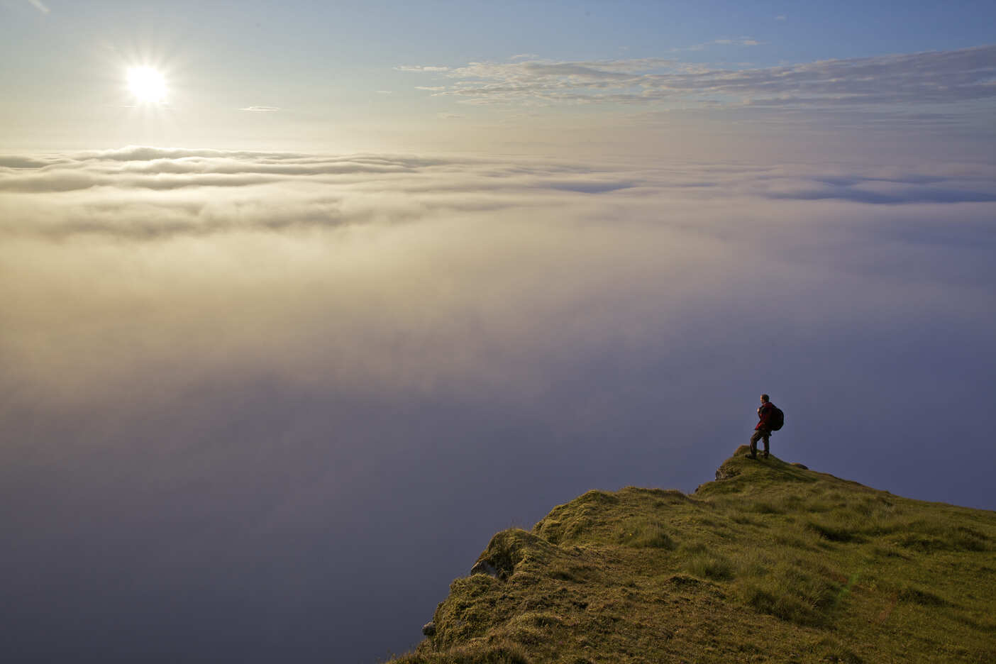 A hiker standing on a slope, overlooking the clouds.