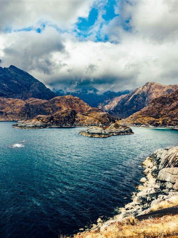 A smiling hiker walking along the shore of Loch Coruisk, the Cuillin Hills in the background