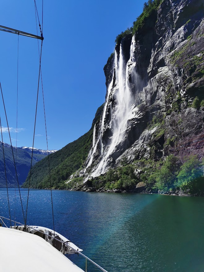 Sailboat passing a waterfall on the Norwegian shoreline