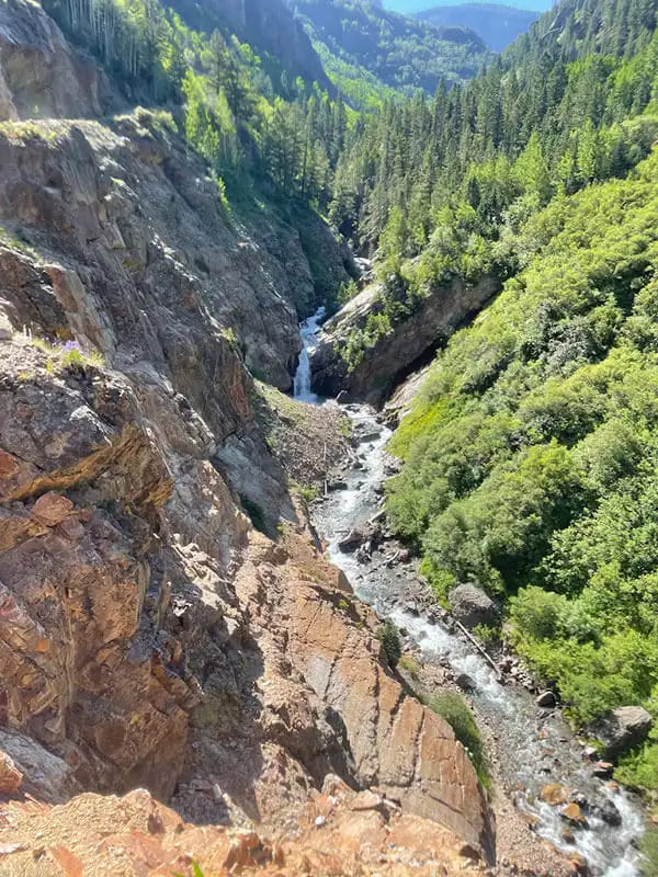 River flowing through the Upper Uncompahgre canyon with granite walls on one side and green shrubbery on the other