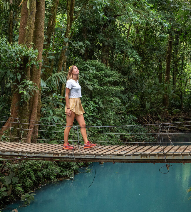 Young woman wandering in tropical rainforest walking on bridge over turquoise lagoon, Costa Rica