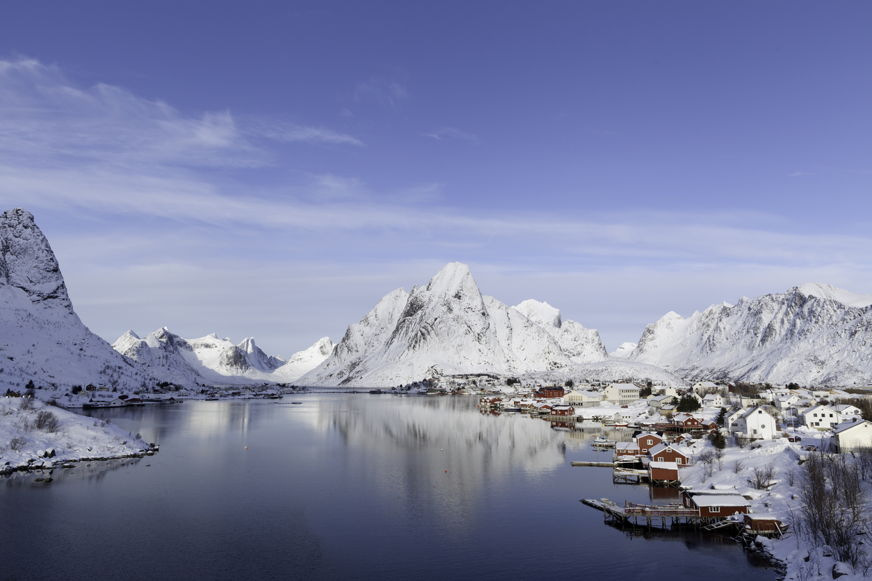 Panorama of a fishing village in Lyngen surrounded by sea and snow-covered mountains.