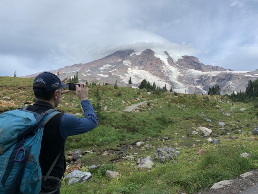 A hiker stops to take photos of Mount Rainier obscured by a lenticular cloud.