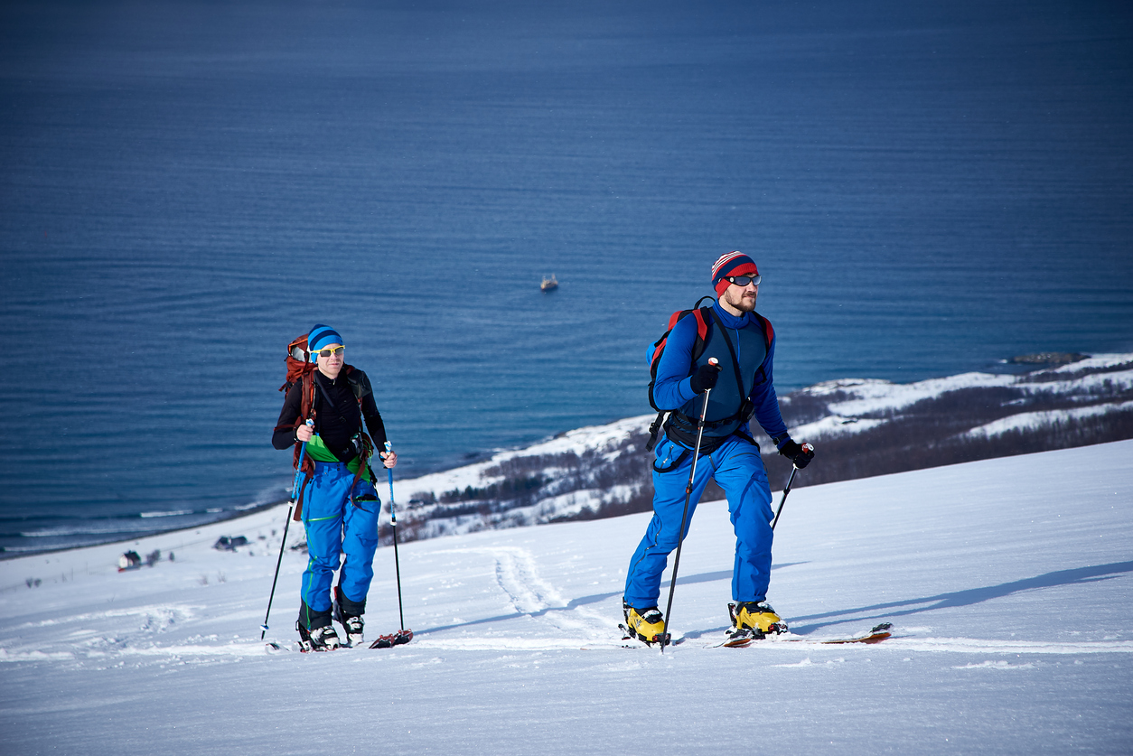 A man and a woman skiing uphill in Lyngen with the ocean in the distance.
