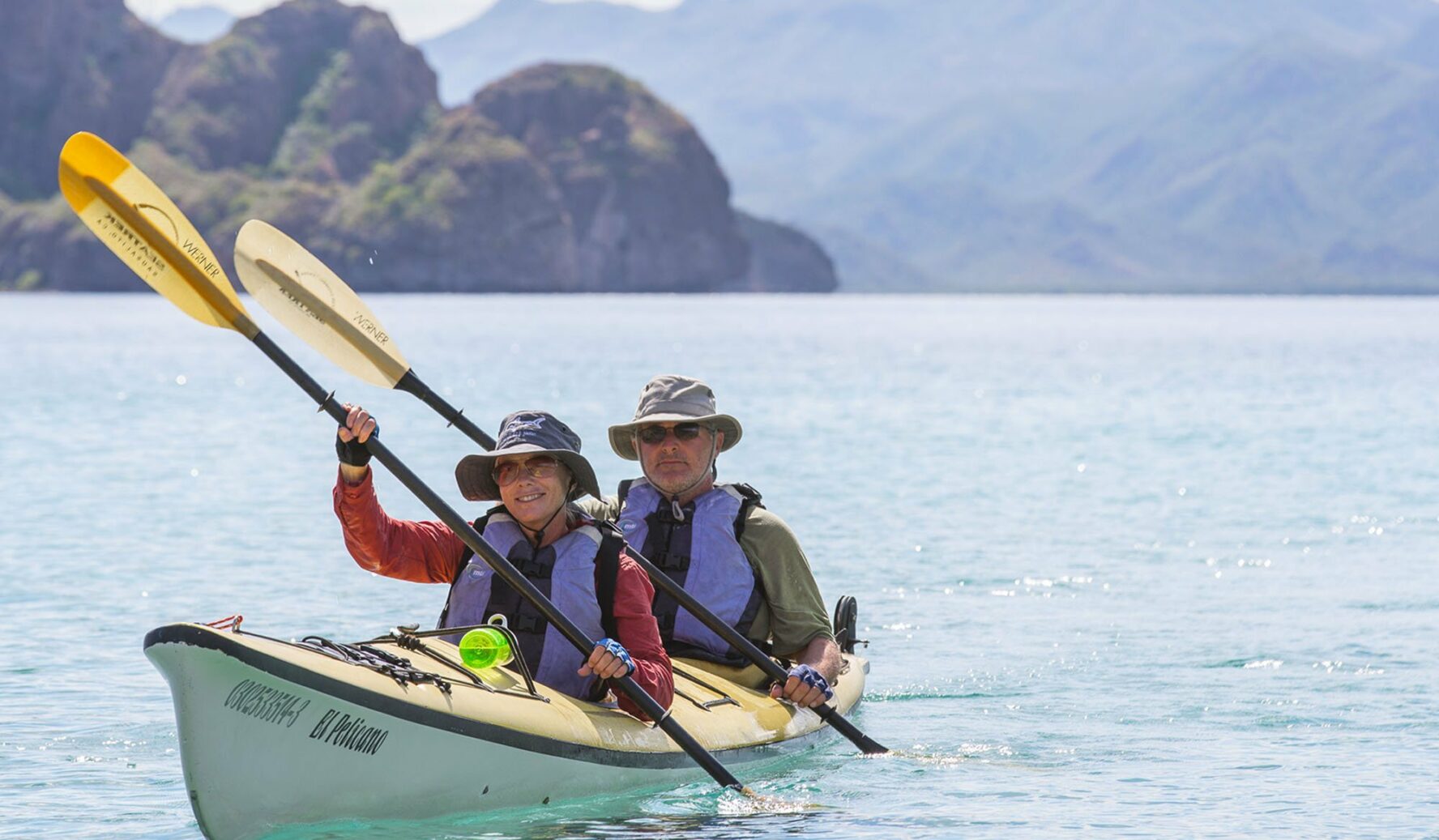 A couple kayaking in the Sea of Cortez in Baja California Sur with mountains in the background and out of focus.