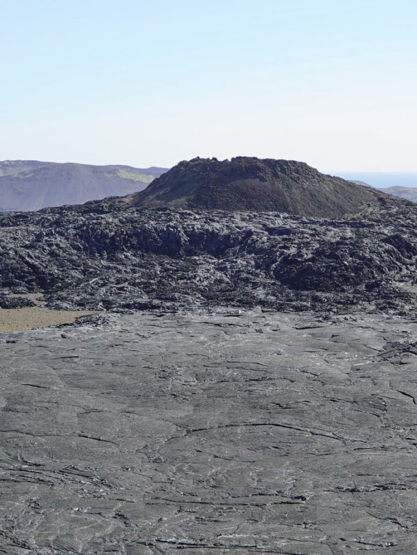 A woman hiking beside the firmed up lava close to the site of an erupting Iceland volcano.