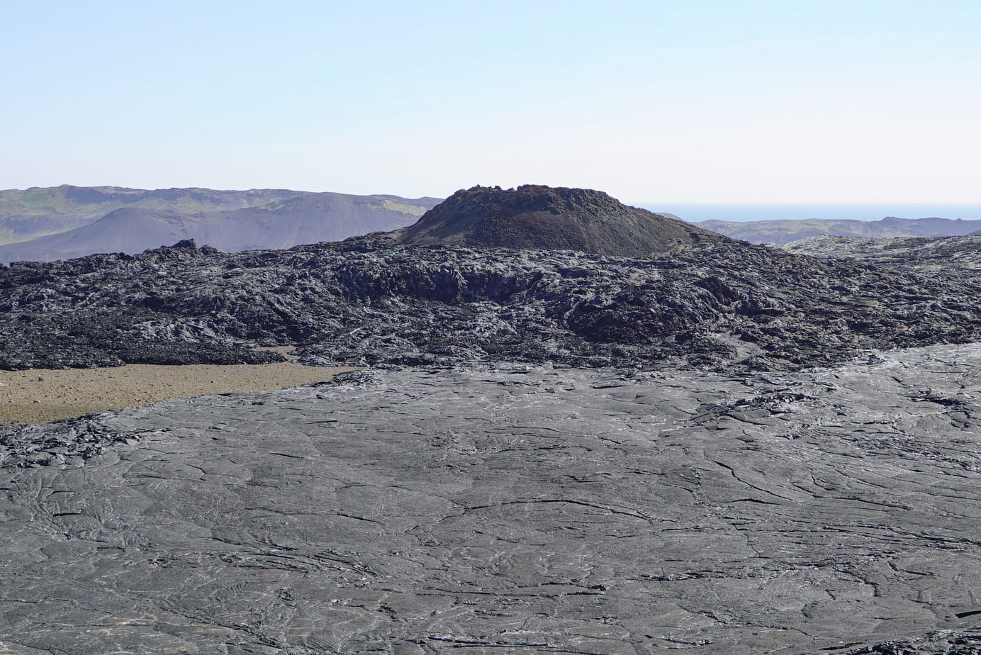 Firmed up lava at the foot of the crater with moss-covered mountains in the distance.