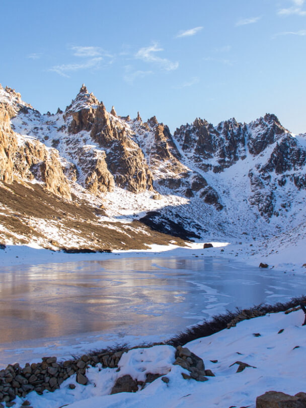 View of a frozen lake encircled by golden granite peaks close to refugio Frey.