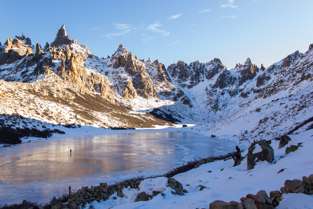 View of a frozen lake encircled by golden granite peaks close to refugio Frey.
