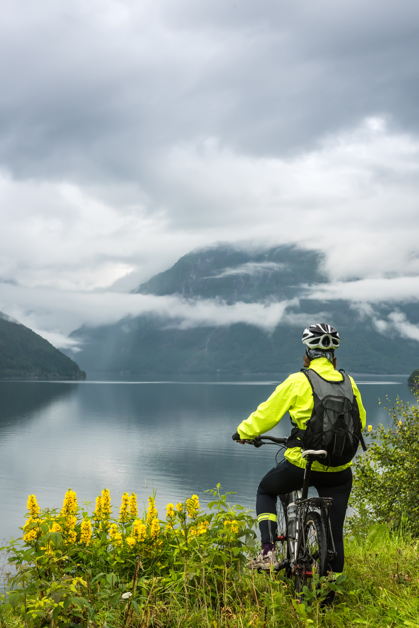 Biker in Norway gazing at a cloud-capped mountain across a long fjord