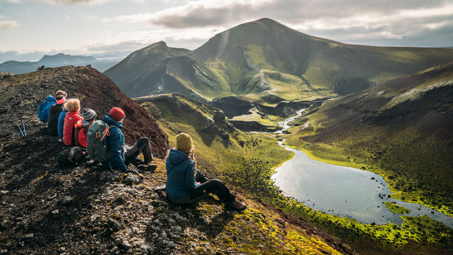 Hikers rest as they gaze upon a lake situated in the dramatic landscape of Iceland.